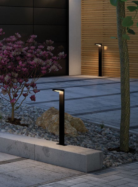 Moderne Wegeleuchten in einem stilvollen Garten bei Nacht mit Steinmauer Kieselsteinen und blühendem Baum
