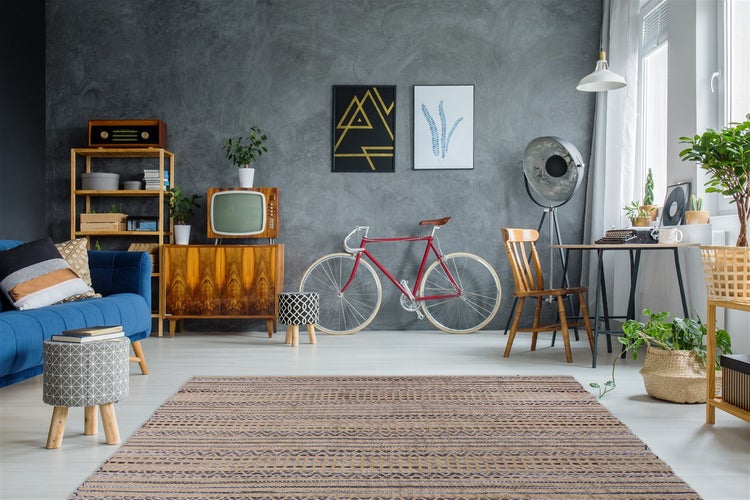 Modernes Wohnzimmer mit grauer Strukturwand, Retro-Möbeln, rotem Fahrrad, blauem Sofa, gemustertem Teppich und industrieller Beleuchtung.