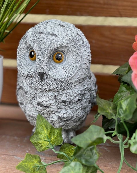 Dekorative Eulen-Gartenfigur in Steinoptik mit detaillierter Federstruktur, platziert zwischen grünen Pflanzen auf Holz.