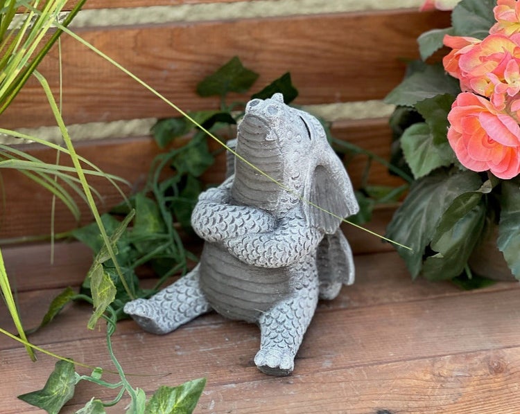 Kleine Drachenfigur aus Stein für den Garten, sitzend und nach oben blickend, dekoriert mit Pflanzen.