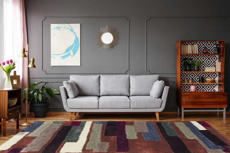 Modern eingerichtetes Wohnzimmer mit grauem Dreisitzer-Sofa, bunt gemustertem Teppich und dunkelgrau gestalteter Wand mit Zierleisten.
