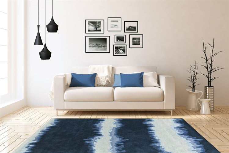 Helles, modernes Wohnzimmer mit hellem Sofa, blauem Teppich mit Wellenmuster, schwarzen Pendelleuchten und einer Bildergalerie an der Wand.