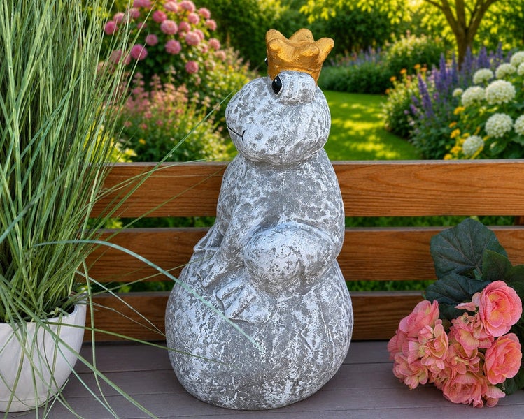 Steinfigur Froschkönig mit Krone als Dekoration für den Garten auf einer Holzbank.