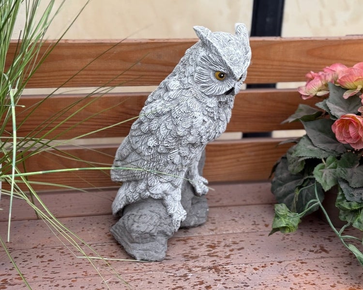 Detaillierte Gartenfigur einer Eule in Steinoptik, platziert auf einer Holzbank.