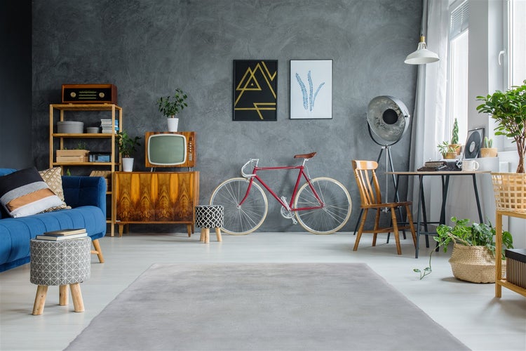 Wohnzimmer im Retro-Stil mit grauer Strukturwand, blauem Sofa, Vintage-Möbeln, einem roten Rennrad und einer großen Studiolampe.