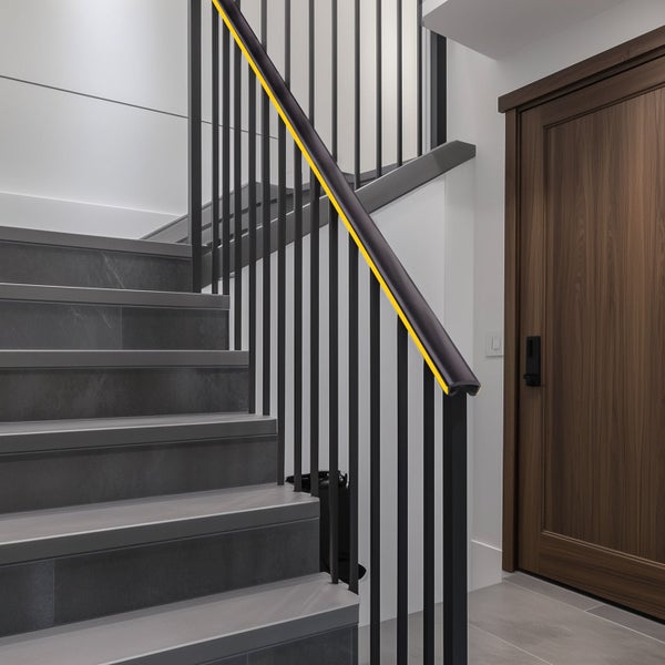 Modernes Treppenhaus mit dunkelgrauen Stufen und schwarzem Handlauf mit integriertem gelbem LED-Lichtstreifen.