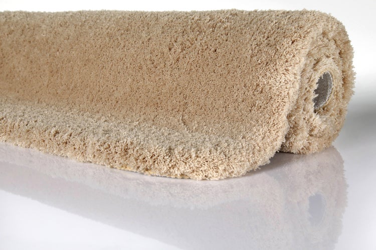 Beiger Hochflor Teppich Shaggy zusammengerollt mit weicher Struktur.