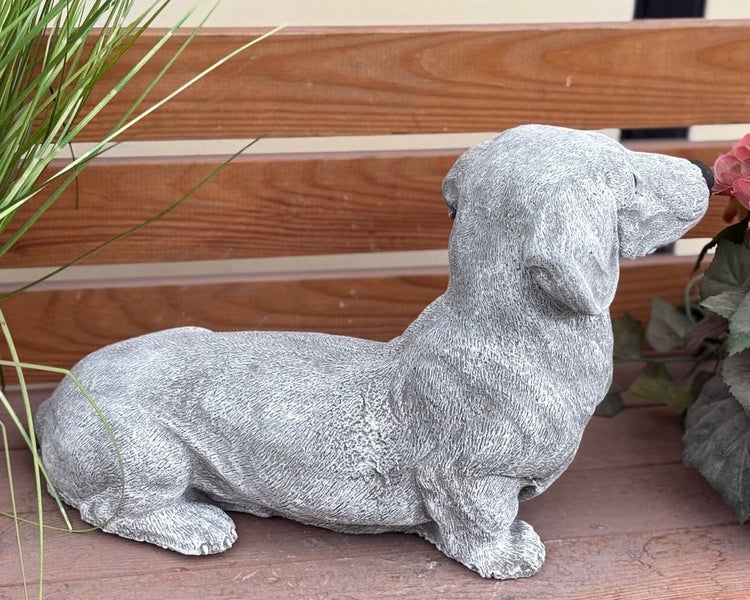 Dackel-Gartenfigur aus Steinguss, liegend auf einer Holzbank für Garten und Terrasse.