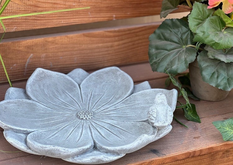 Vogeltränke aus Beton in Blütenform mit kleinem Vogel als Verzierung für den Garten.