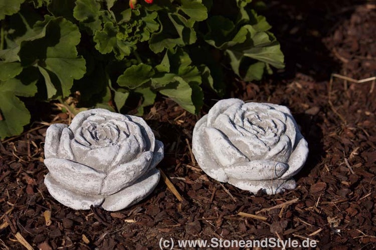Zwei dekorative Rosenblüten aus Stein zur Gartendekoration auf Rindenmulch