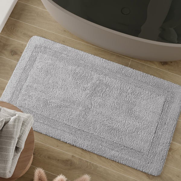 Rechteckiger Badteppich mit Webkante vor einer Badewanne auf Holzboden im modernen Badezimmer.