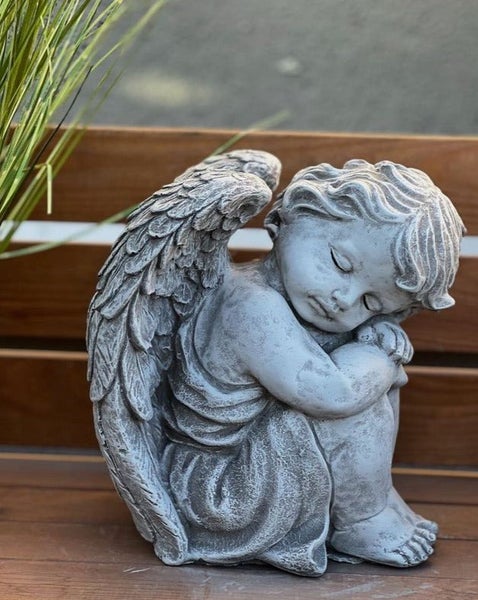 Schlafende Engel-Statue aus grauem Stein, sitzende Engelsfigur mit Flügeln als Garten- oder Grabdekoration.