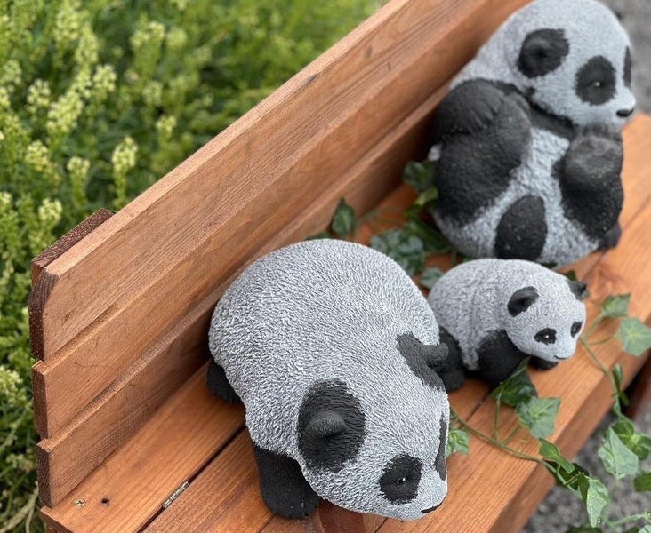 Drei dekorative Pandafiguren aus Kunststein zur Dekoration im Garten auf einer Holzbank.