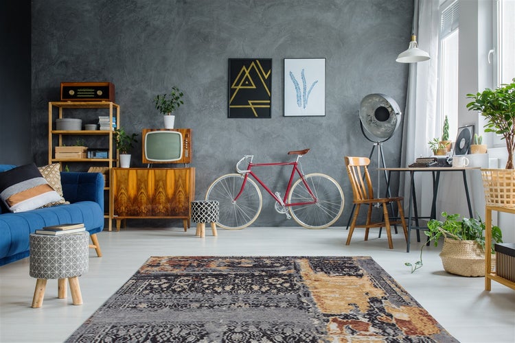 Modern eingerichtetes Wohnzimmer mit grauer Wand in Betonoptik, blauem Sofa, Vintage-Möbeln, rotem Fahrrad und einem gemusterten Teppich.