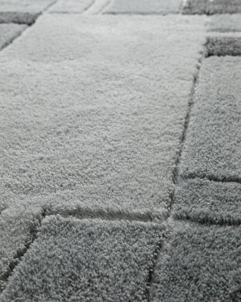 Hochflor-Teppich in Grau mit geometrischem Muster, Detailaufnahme der weichen Struktur.