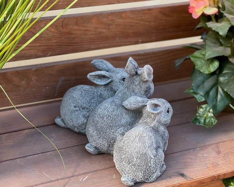 Drei dekorative Hasenfiguren aus Steinoptik zur Garten- oder Terrassendekoration auf einer Holzbank.