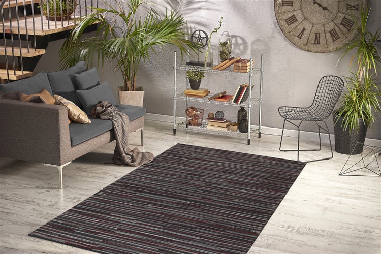 Gestreifter Teppich in modernem Wohnzimmer mit grauem Sofa, Metallregal, Drahtstuhl und Zimmerpflanzen auf hellem Bodenbelag.