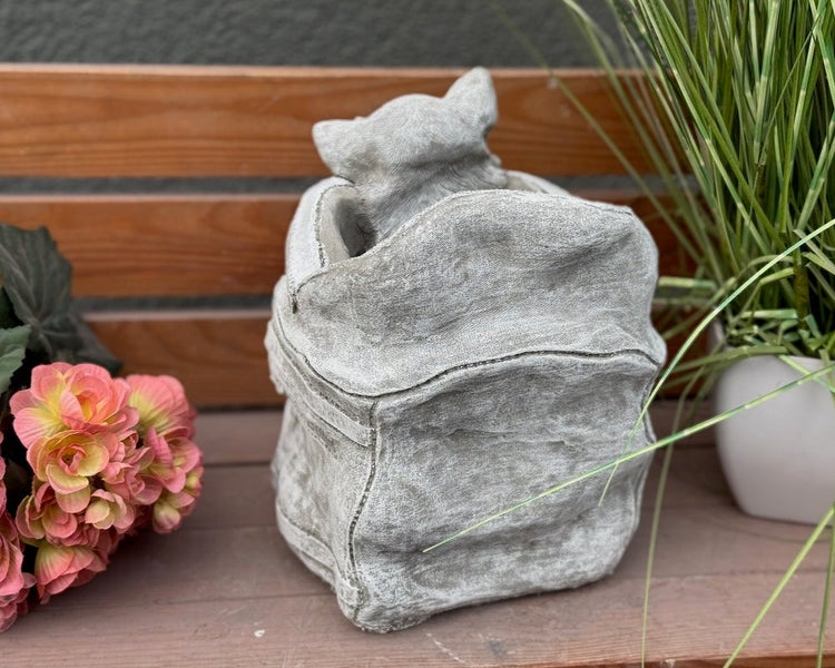 Gartenfigur aus Steinguss in Form einer kleinen Katze in einem Sack, dekoriert auf einer Holzbank.