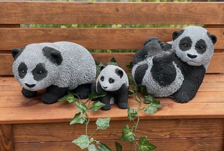 Drei Panda Figuren aus Kunststein zur Gartendekoration auf einer hölzernen Bank mit Efeuranke.