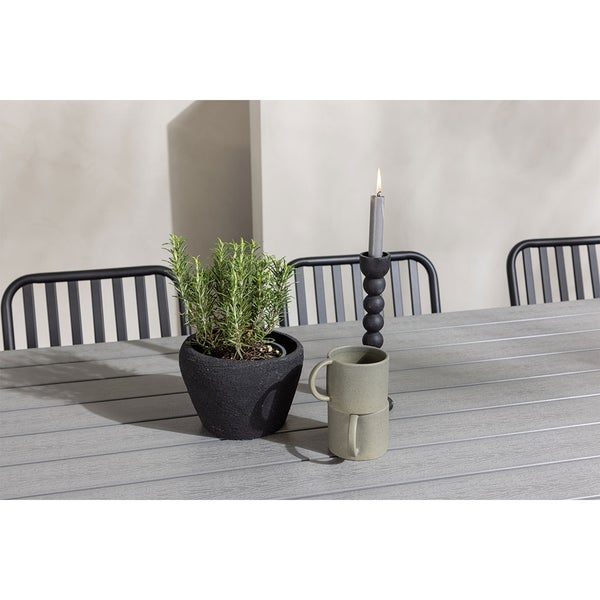 Dekoration mit Topfpflanze, Kerzenständer mit Kerze und zwei übereinander gestapelten Bechern auf einem Gartentisch