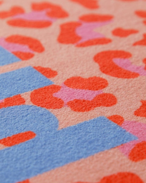 Nahaufnahme eines weichen Teppichs mit einem Tiermuster in Blau, Rosa und Orange.