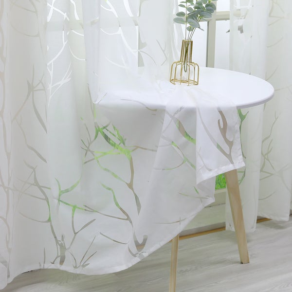Transparenter Vorhang mit Zweigmuster neben einem Tisch