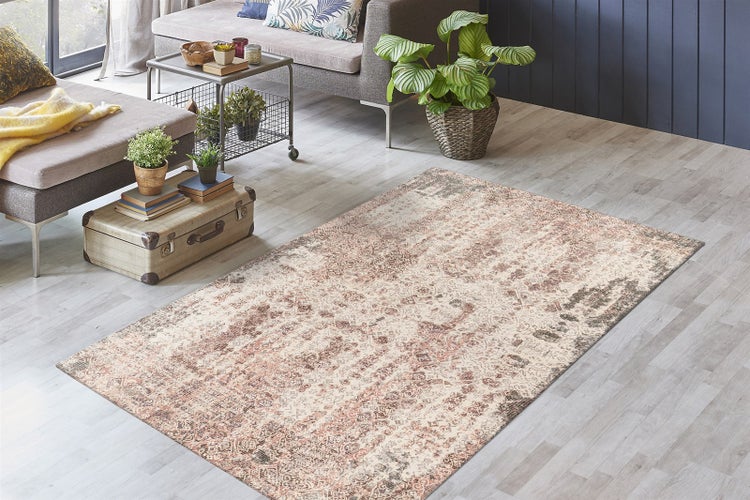 Rechteckiger Teppich mit beige-braunem Orient-Muster im Vintage-Stil in einem hellen Wohnzimmer mit grauem Sofa und Zimmerpflanzen.