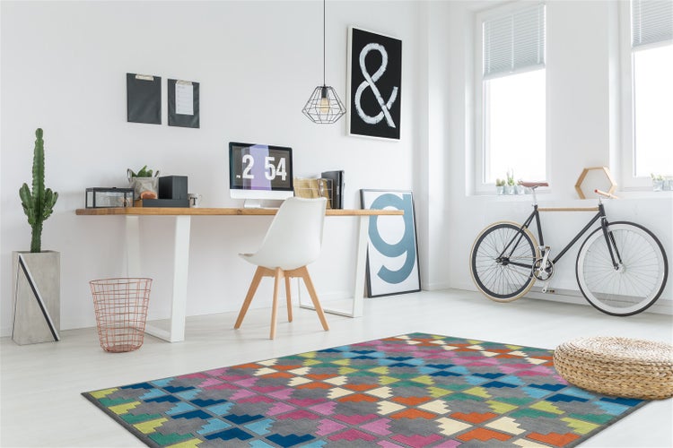 Helles, modernes Arbeitszimmer mit Holzschreibtisch, weißem Stuhl, buntem Teppich mit geometrischem Muster und einem Fahrrad.