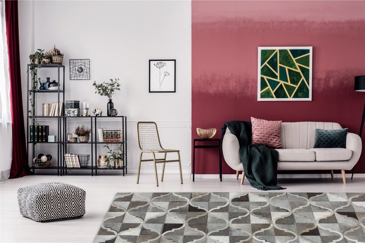 Modernes Wohnzimmer mit beige Sofa, Wand mit rotem Farbverlauf, schwarzem Metallregal, goldenem Metallstuhl und gemustertem Teppich.