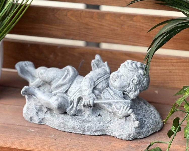 Gartenfigur Putto aus Stein, liegender Engel mit Geige zur Dekoration im Garten.