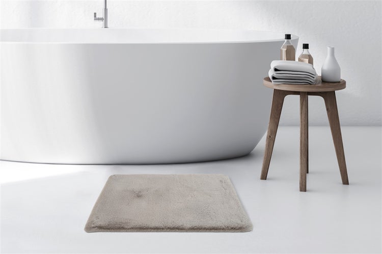 Flauschige Badematte vor einer freistehenden Badewanne in einem hellen, modernen Badezimmer mit Holzschemel und Handtüchern.