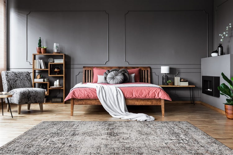 Modernes Schlafzimmer mit Holzbett, grauem Sessel, gemustertem Teppich, Wandleisten an grauen Wänden und Holzfußboden.