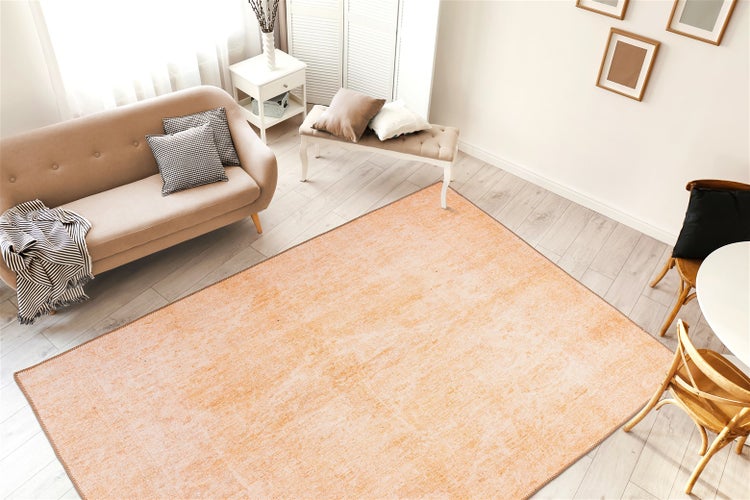 Rechteckiger Teppich in hellem Orange mit Used-Look in einem modern eingerichteten, hellen Wohnzimmer mit Sofa und Holzfußboden.