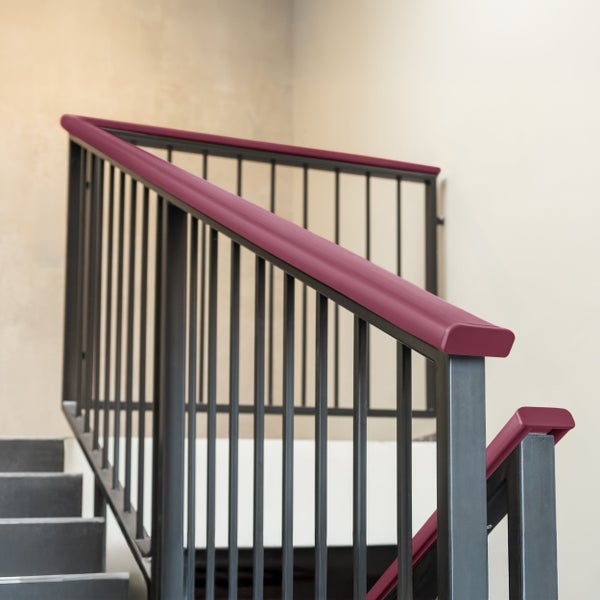 Moderne Treppe mit dunklem Metallgeländer, vertikalen Stäben und einem beerenfarbenen Handlauf-Überzug.