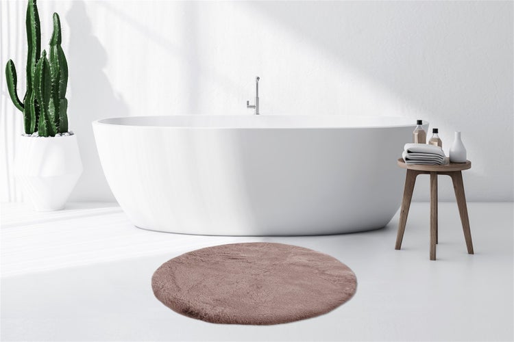 Helles Badezimmer mit freistehender Badewanne, einem runden Badeteppich, einem Kaktus im Topf und einem Holzschemel mit Handtüchern.