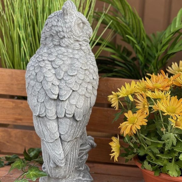 Dekorative Eulenfigur aus Stein für den Garten, detailreiche Darstellung in natürlicher Optik auf einem Holzuntergrund mit Blumen.