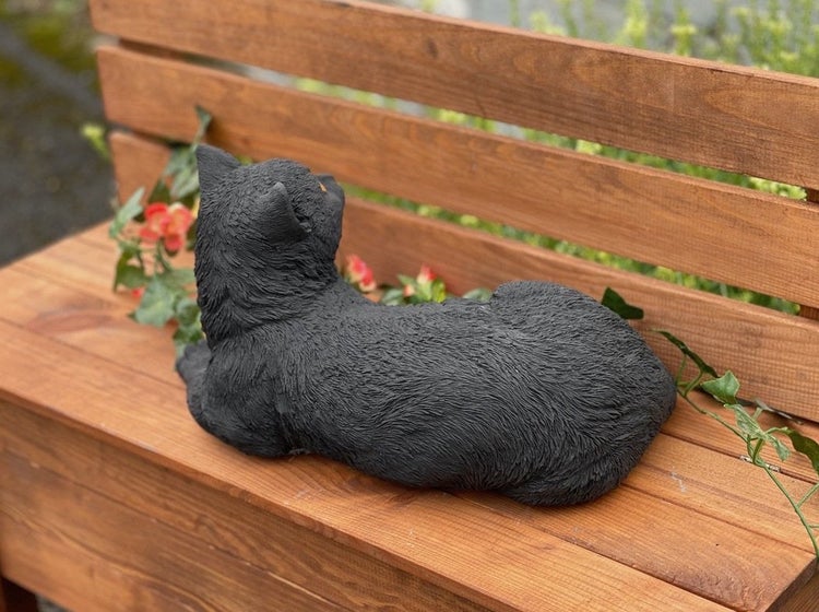 Dekorative Gartenfigur Katze liegend auf einer Holzbank mit künstlichen Ranken für die Gartendekoration