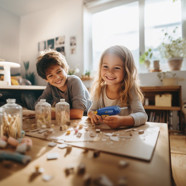 Zwei Kinder basteln gemeinsam mit einer Steinel Heißklebepistole an einem Holztisch in einem hellen, freundlichen Wohnraum.
