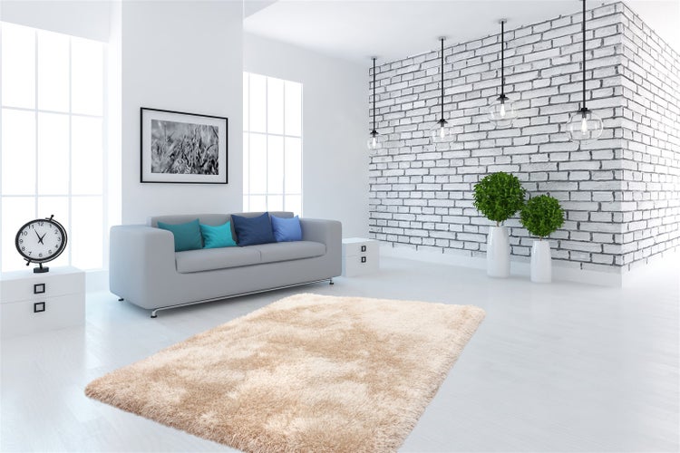 Modernes Wohnzimmer mit hellem Hochflor-Teppich, grauem Sofa vor weißer Ziegelwand und dekorativen Hängelampen.