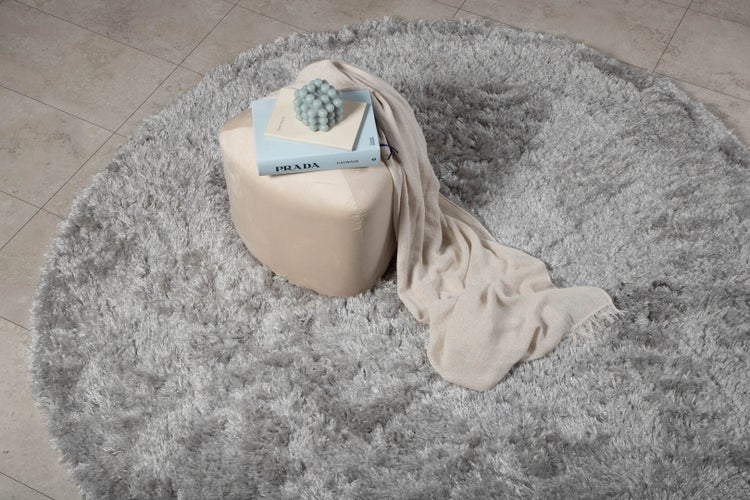 Ein silberfarbener Teppich mit einem Hocker, einem Buch und einer Decke.