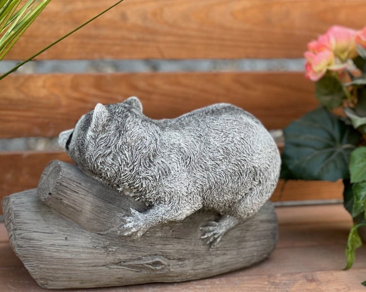 Gartenfigur Waschbär auf einem Baumstamm liegend, detailreiche Tierfigur für den Außenbereich.