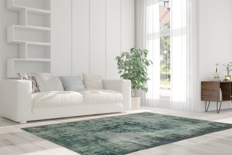 Helles, modernes Wohnzimmer mit grün-blau gemustertem Teppich auf hellem Holzboden, weißem Sofa, Zimmerpflanze und großen Fenstern.