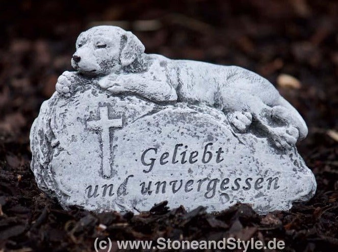 Grabschmuck für Haustiere als liegender Hund auf einem Stein mit Kreuz und Inschrift Geliebt und unvergessen aus Steinguss für den Garten.