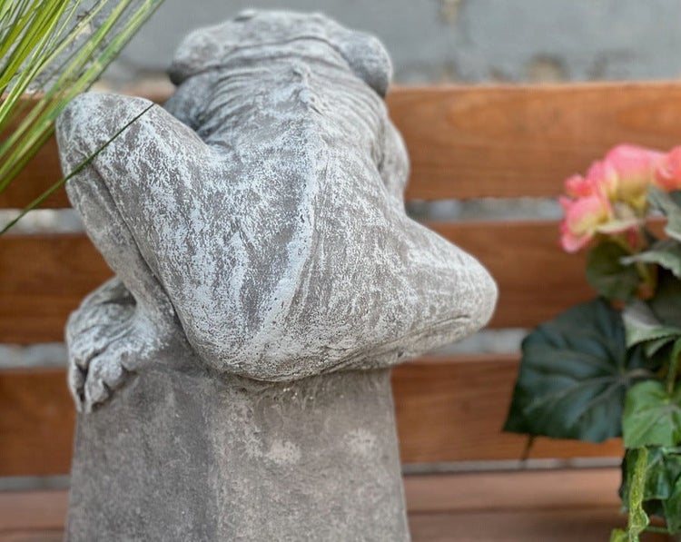 Gartenfigur eines Frosches aus Stein von hinten gesehen, sitzend auf einem Sockel.