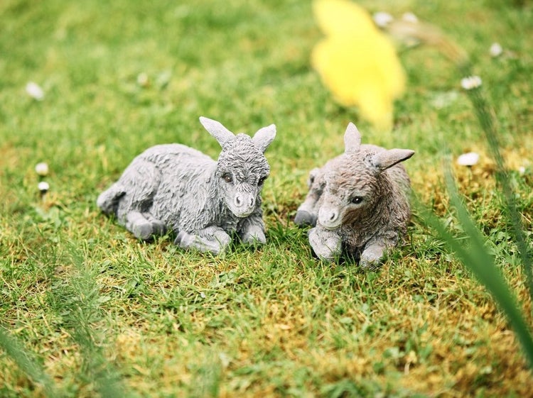 Zwei liegende Esel Figuren aus Kunststein zur Dekoration im Garten auf einer Wiese.