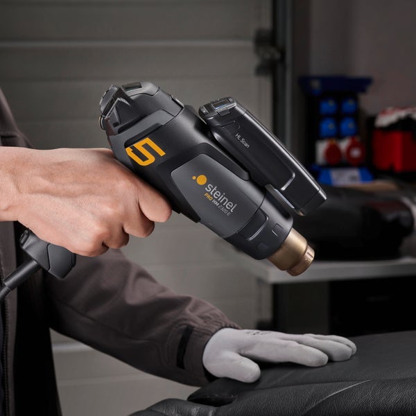 Eine Person hält eine Steinel Heißluftgebläse HG 2320 E mit HL Scan Aufsatz in der Hand und arbeitet an einem Gegenstand.