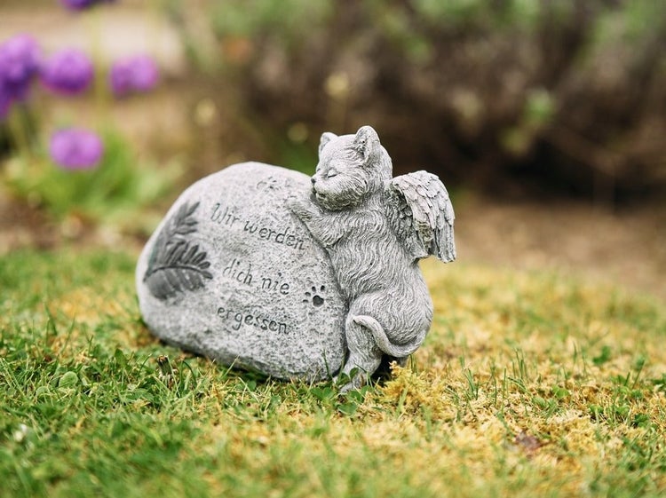 Grabschmuck in Form eines Steins mit einer Katzenfigur mit Engelsflügeln und der Aufschrift Wir werden dich nie vergessen zur Gartendekoration.