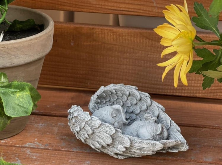 Dekorative Gartenfigur in Form eines schlafenden Engels, der von Flügeln umhüllt ist, aus wetterfestem Material, als Grabschmuck oder Dekoration.