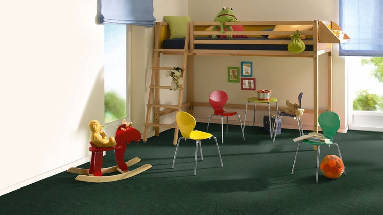 Helles Kinderzimmer mit dunkelgrünem Teppichboden, einem Hochbett aus Holz, bunten Stühlen und einem Schaukelelch.