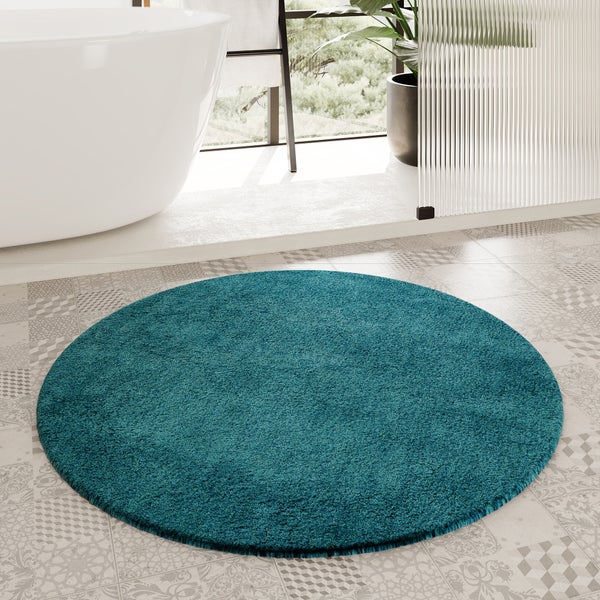Runde Badematte in Türkis auf gemusterten Fliesen in einem hellen, modernen Badezimmer neben einer freistehenden Badewanne.